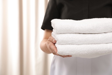 Photo of Young maid holding stack of fresh towels in hotel room, closeup. Space for text