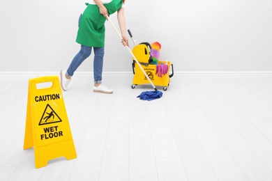 Photo of Safety sign with phrase "CAUTION WET FLOOR" and young woman cleaning, indoors