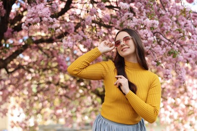 Beautiful woman in sunglasses near blossoming tree on spring day, space for text