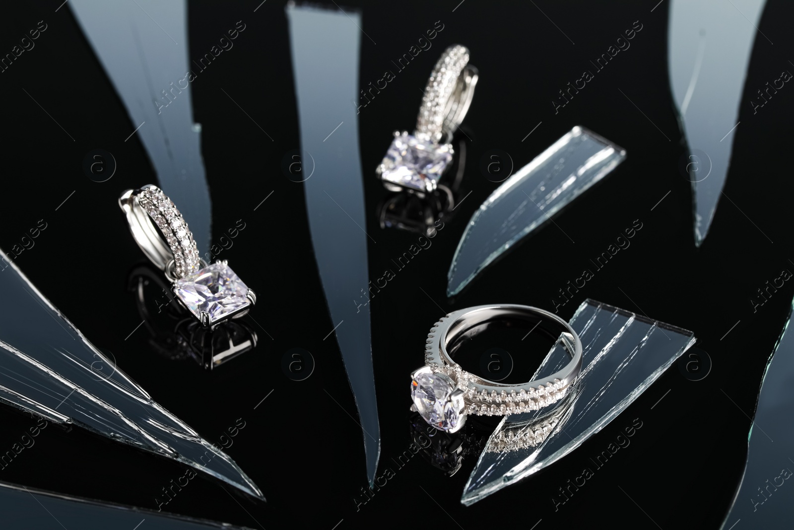 Photo of Luxury jewelry. Stylish presentation of elegant ring and earrings on black mirror surface with broken glass