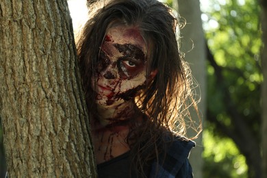 Photo of Scary zombie near tree outdoors. Halloween monster