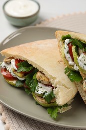 Photo of Delicious pita sandwiches with grilled vegetables and sour cream sauce on table, closeup