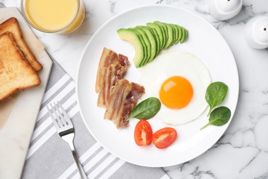 Photo of Tasty breakfast with fried egg, bacon and avocado served on white marble table, flat lay