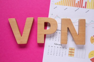 Photo of Acronym VPN made of wooden letters and calendar with statistics diagram on crimson background, flat lay