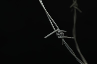 Metal barbed wire on black background, closeup. Space for text