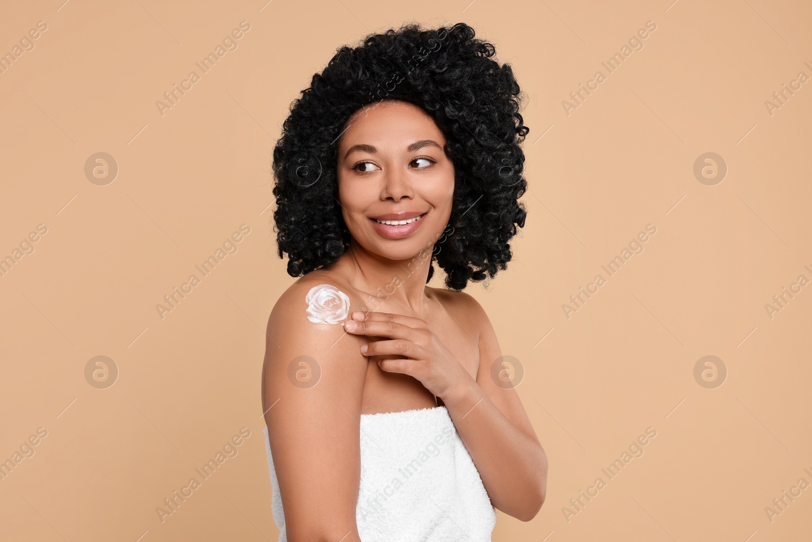 Photo of Young woman applying body cream onto shoulder on beige background