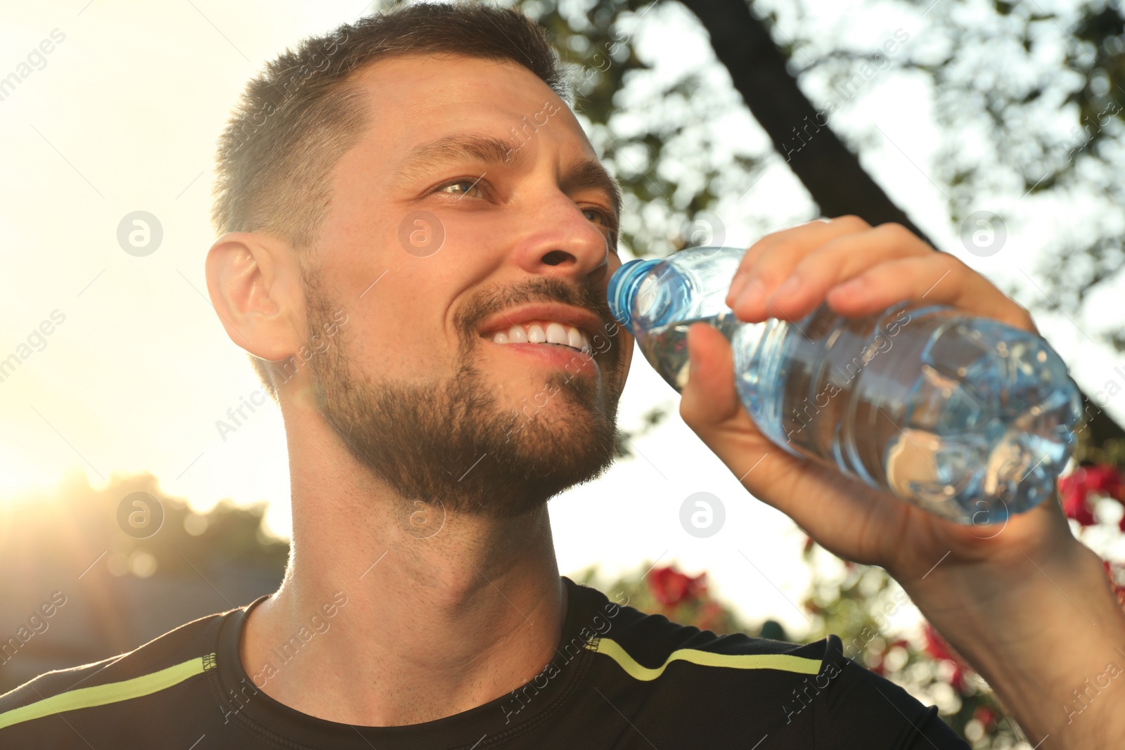 Photo of Happy man drinking water outdoors on hot summer day. Refreshing drink