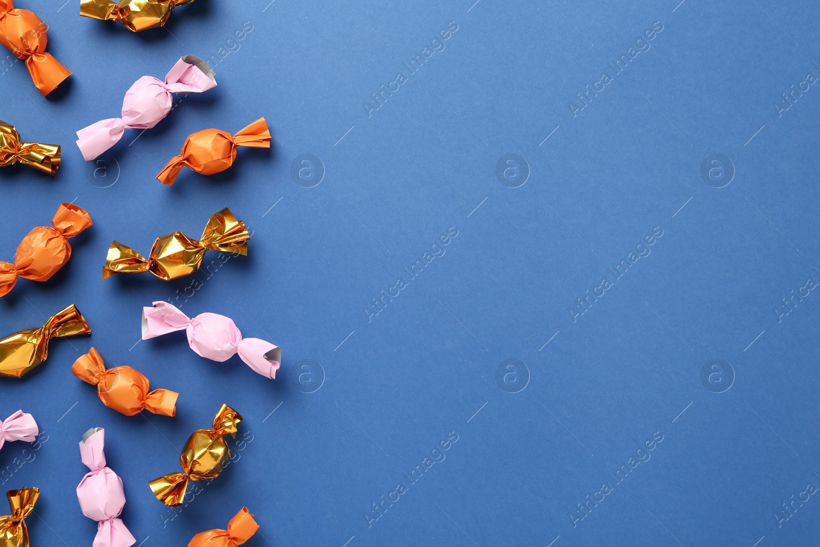 Photo of Many candies in colorful wrappers on blue background, flat lay. Space for text