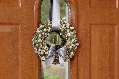 Wreath made of beautiful willow branches and grey bow on wooden door