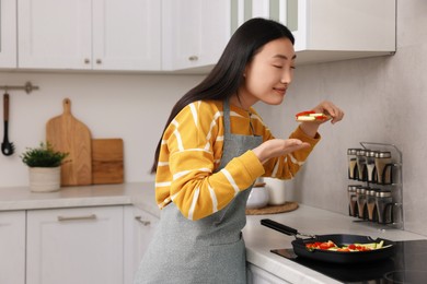 Photo of Beautiful woman cooking and smelling vegetable dish in kitchen. Space for text