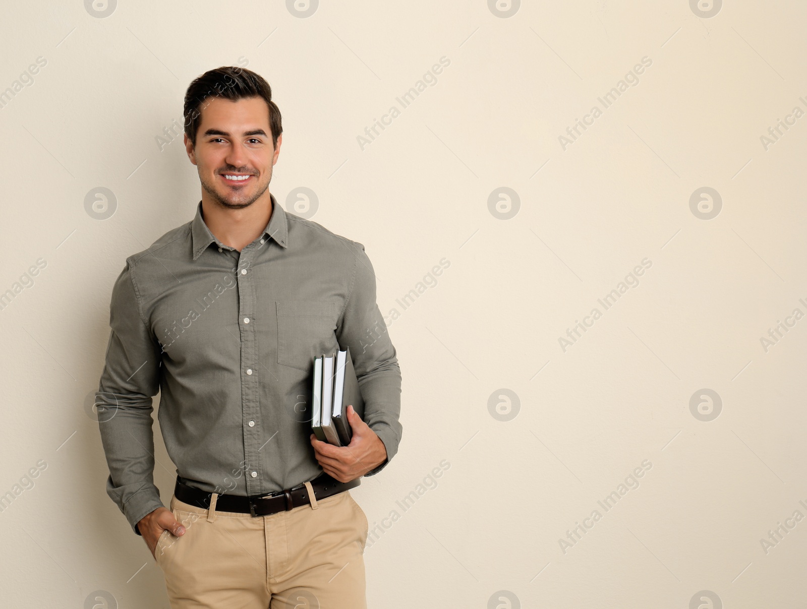 Photo of Young male teacher with books on beige background. Space for text