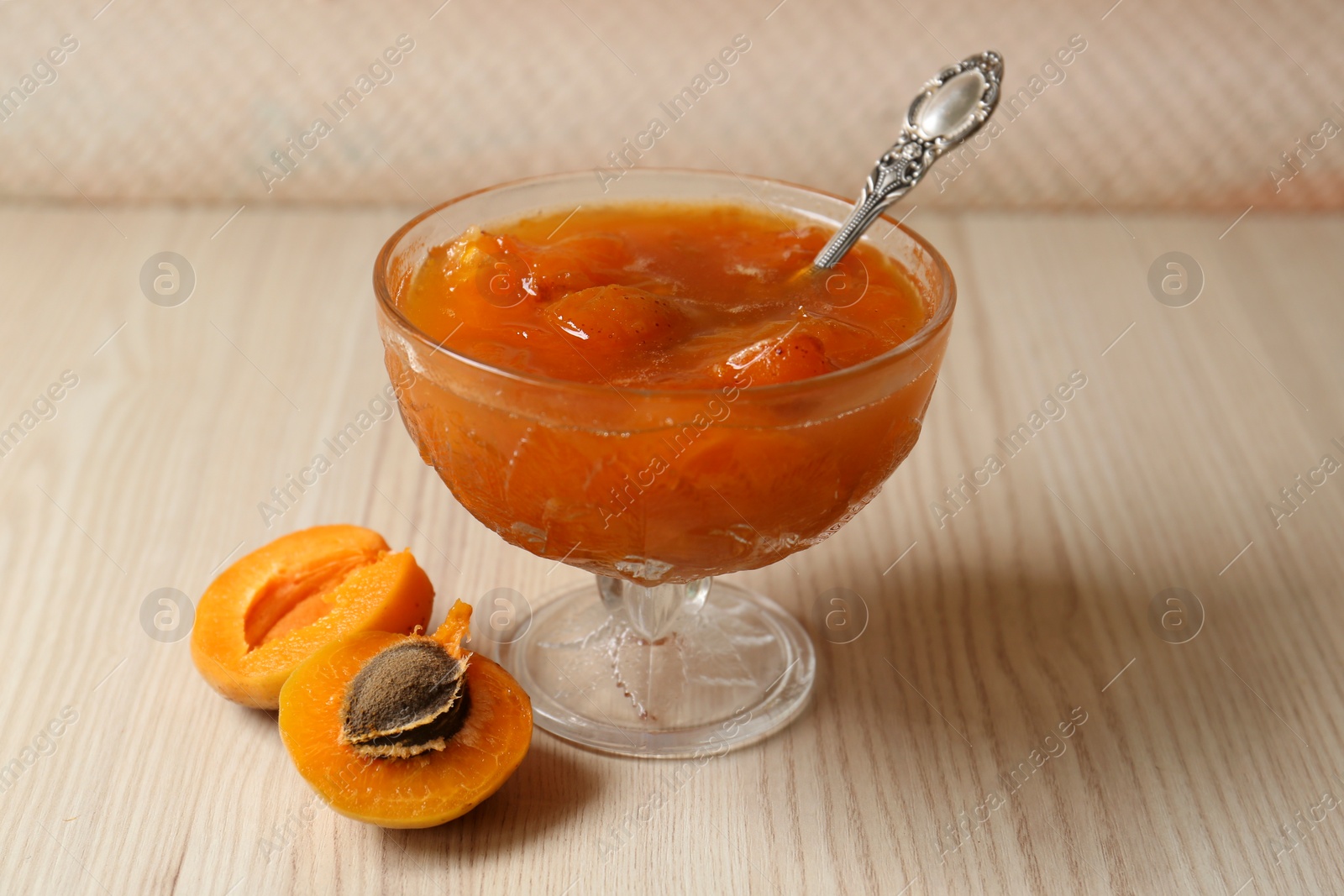 Photo of Dessert bowl with delicious apricot jam and spoon on white wooden table