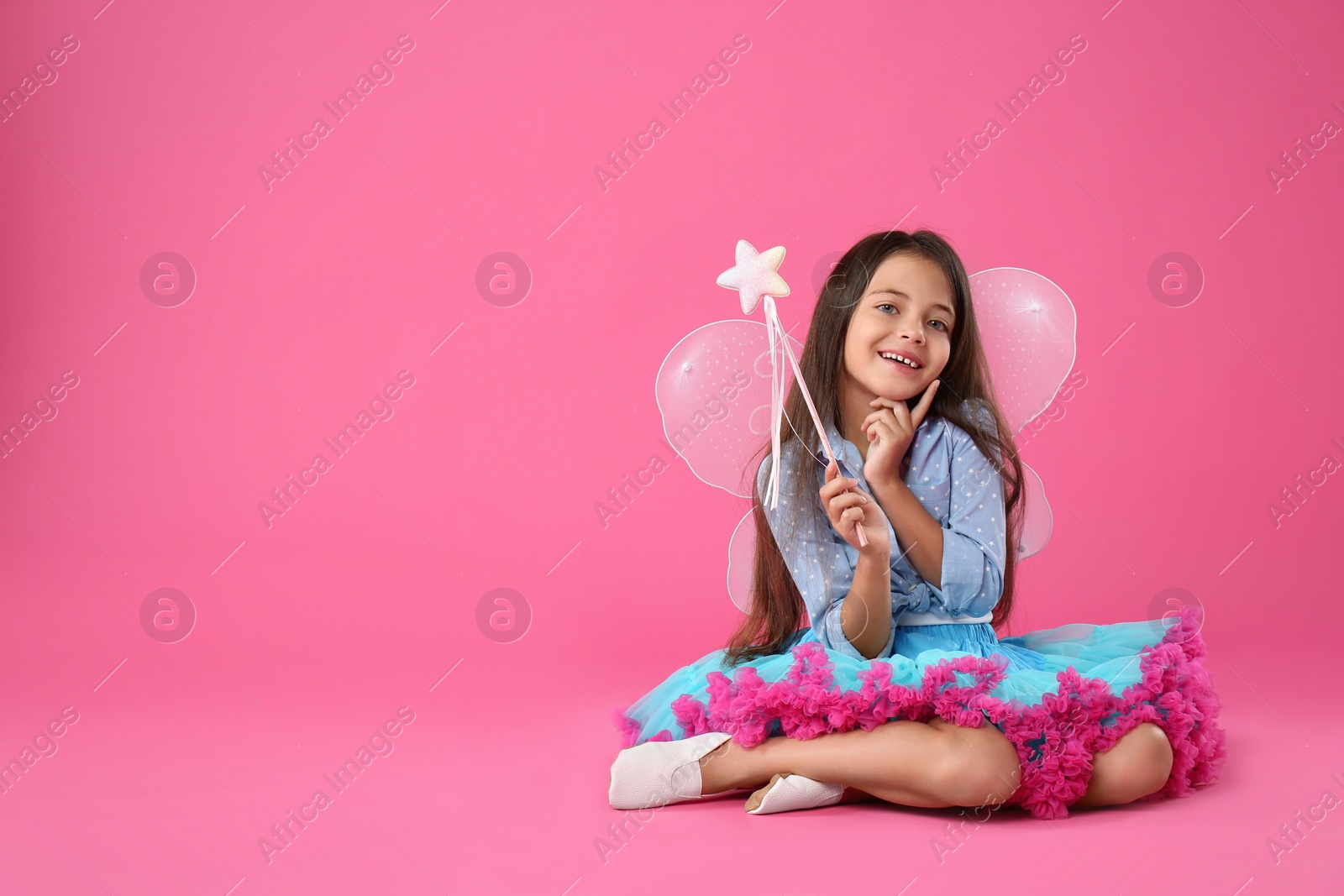 Photo of Cute little girl in fairy costume with wings and magic wand on pink background. Space for text