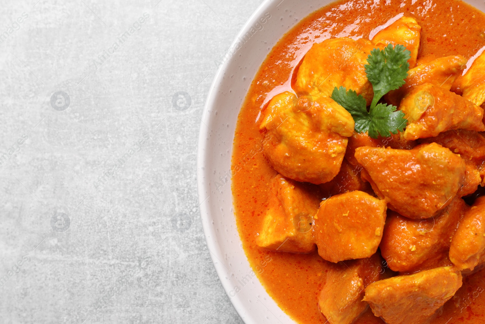 Photo of Bowl of delicious chicken curry on light grey table, top view. Space for text