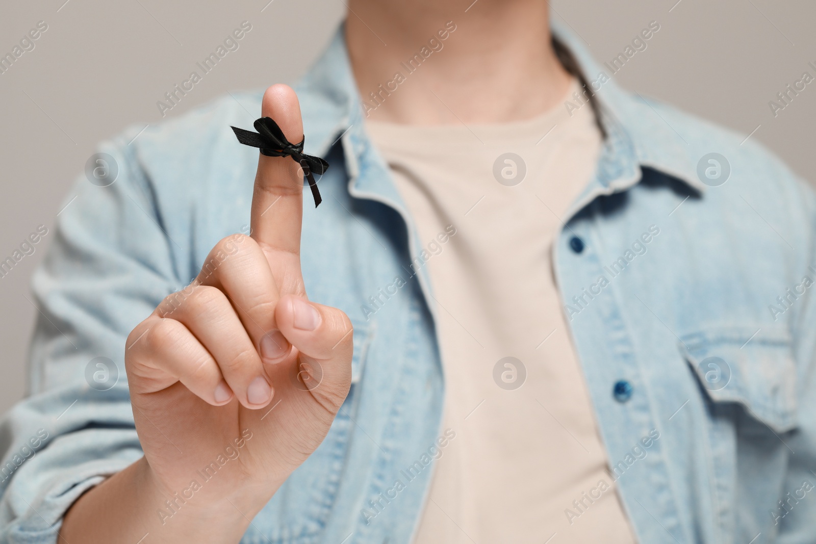 Photo of Man showing index finger with tied bow as reminder against light grey background, focus on hand