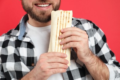 Photo of Young man with delicious shawarma on red background, closeup