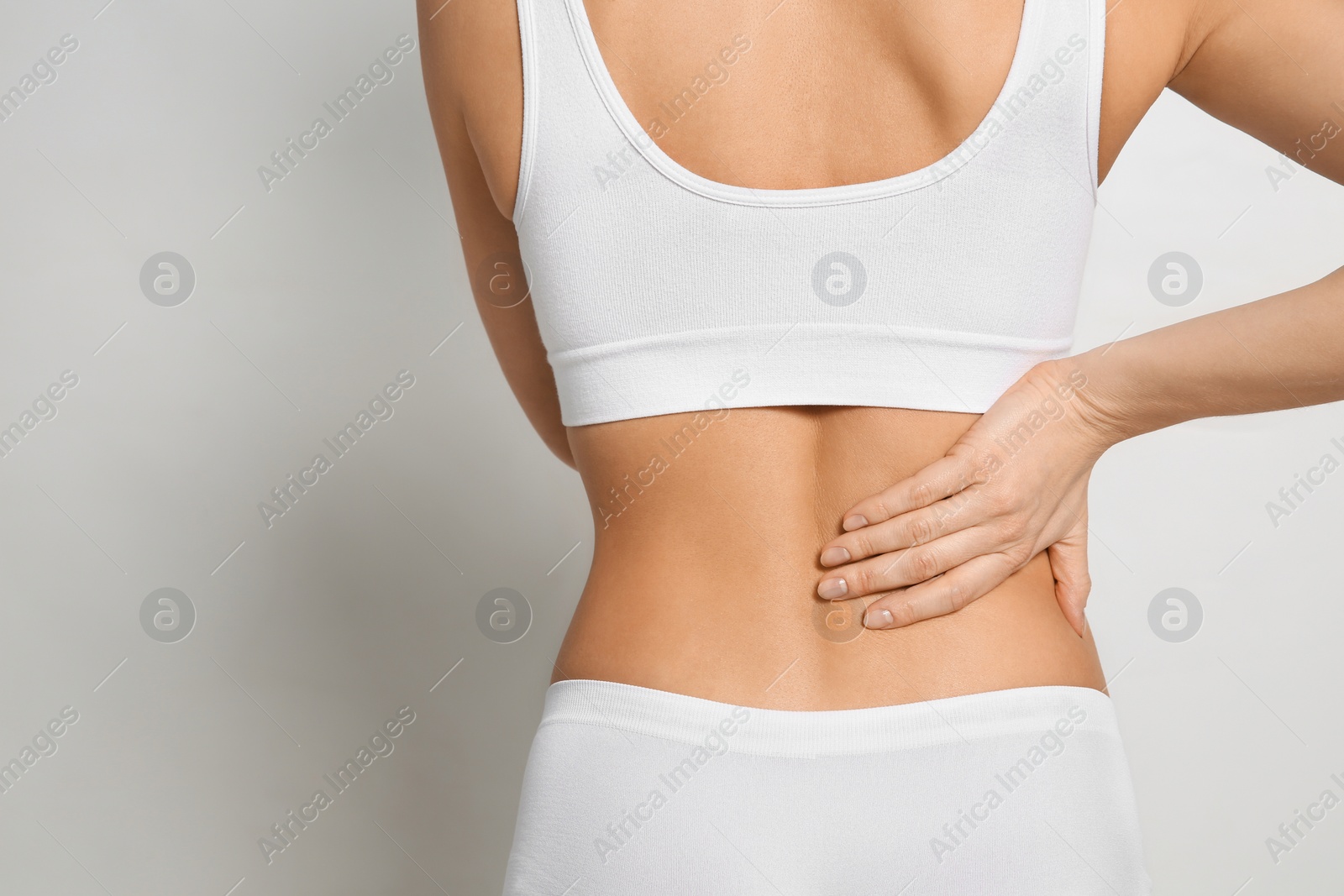 Photo of Woman suffering from pain in back on light grey background, closeup. Space for text