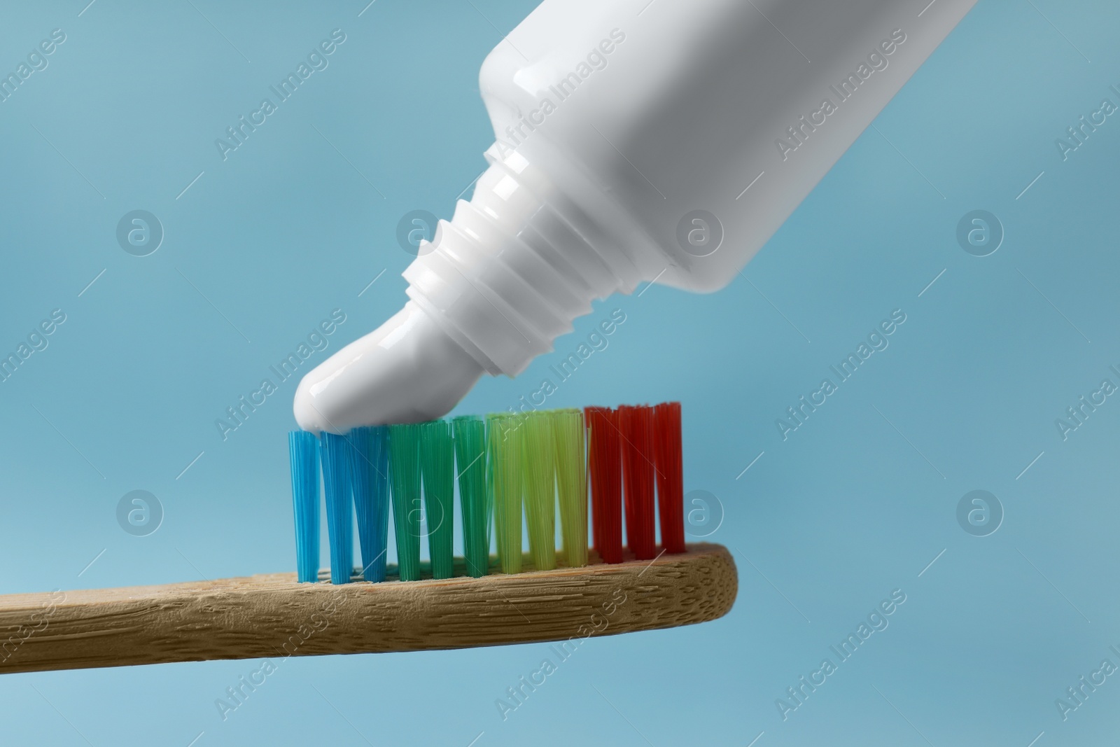 Photo of Squeezing toothpaste onto brush against light blue background, closeup