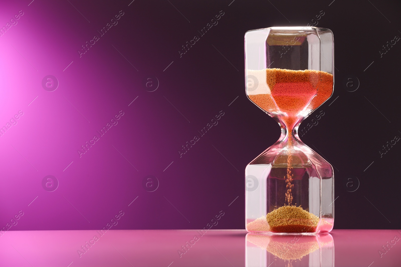 Photo of Hourglass with flowing sand on color background. Space for text