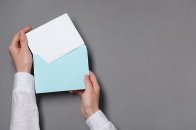 Woman taking card out of letter envelope at grey table, top view. Space for text