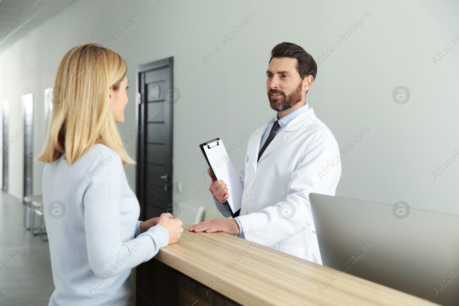 Photo of Doctor with clipboard consulting patient in clinic