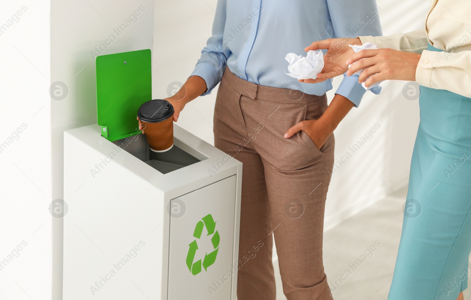 Photo of Young women throwing garbage into recycling bin in office, closeup