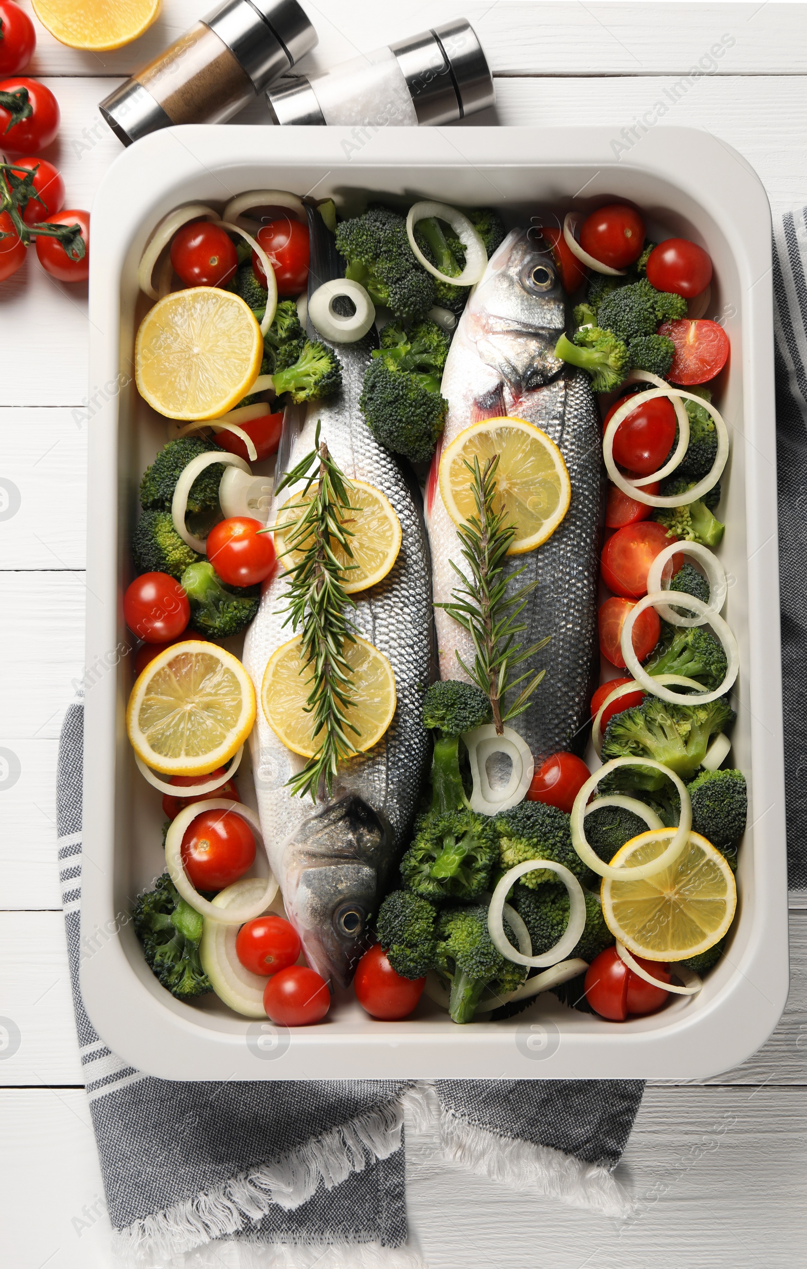 Photo of Raw fish with vegetables and lemon in baking dish on white wooden table, flat lay