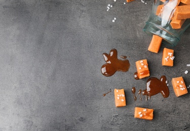 Delicious caramel candies with sauce and salt on gray background