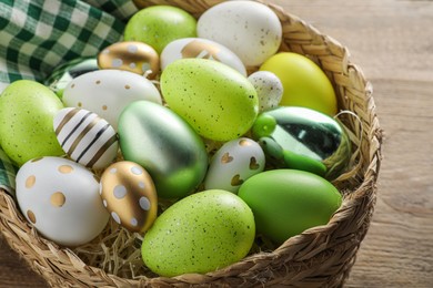 Photo of Many beautifully decorated Easter eggs in wicker basket on wooden table, closeup