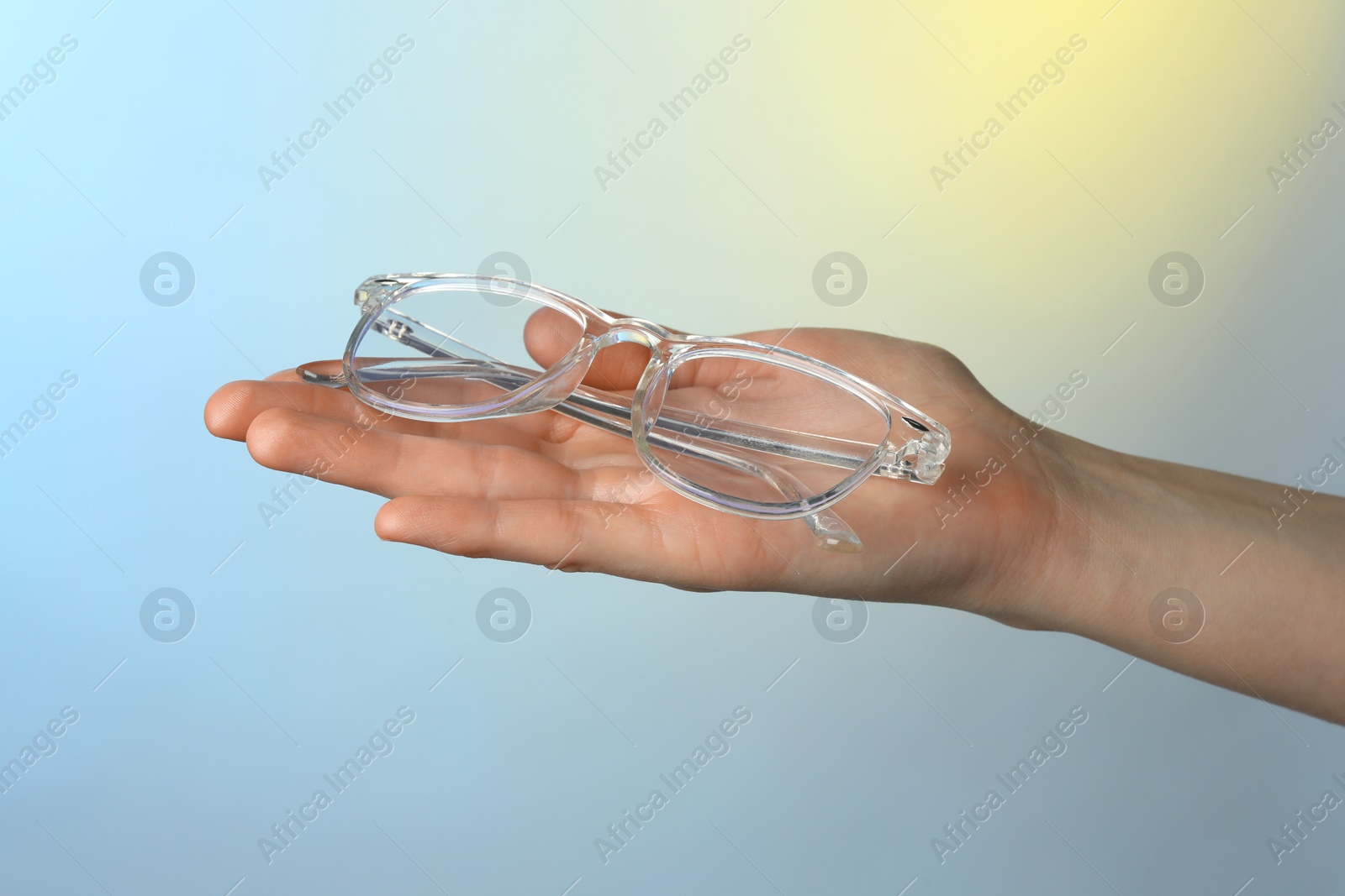 Photo of Woman holding glasses with transparent frame on color background, closeup