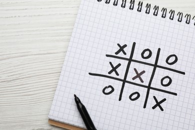 Photo of Notebook with tic tac toe game and marker on white wooden table, top view