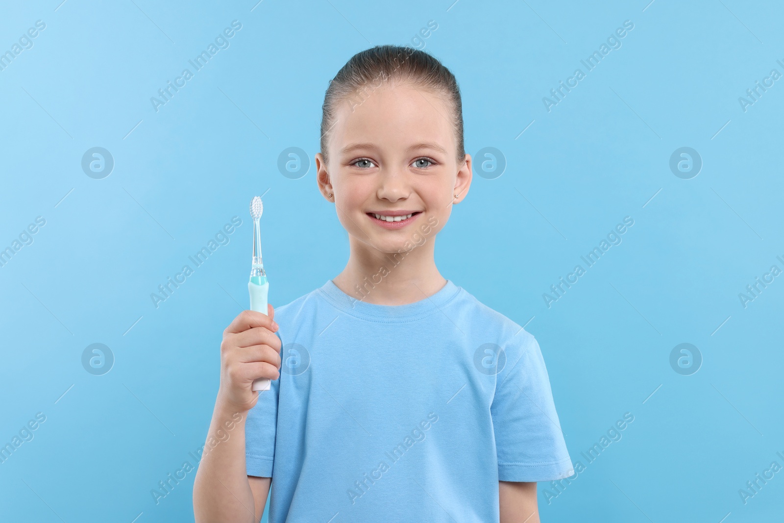 Photo of Happy girl holding electric toothbrush on light blue background