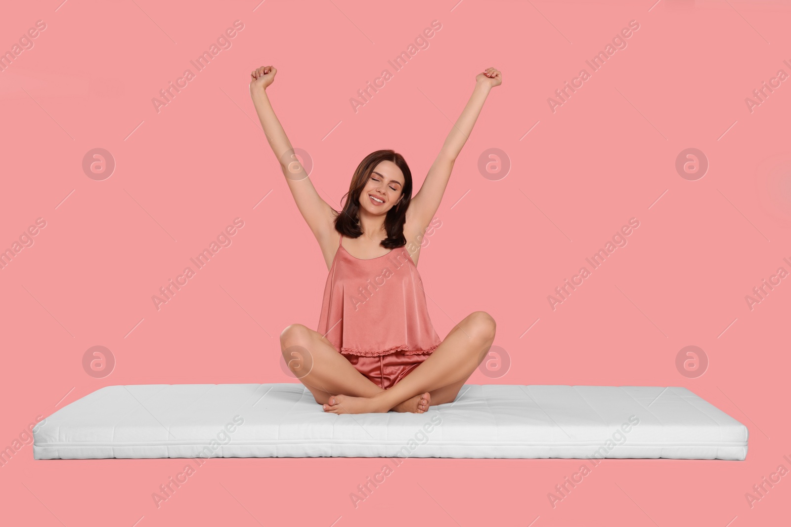 Photo of Young woman stretching on soft mattress against pale pink background