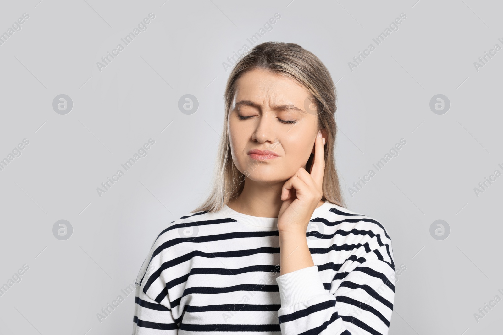 Photo of Young woman suffering from ear pain on light grey background