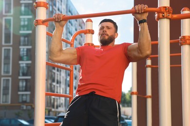 Photo of Man training on horizontal bar at outdoor gym on sunny day