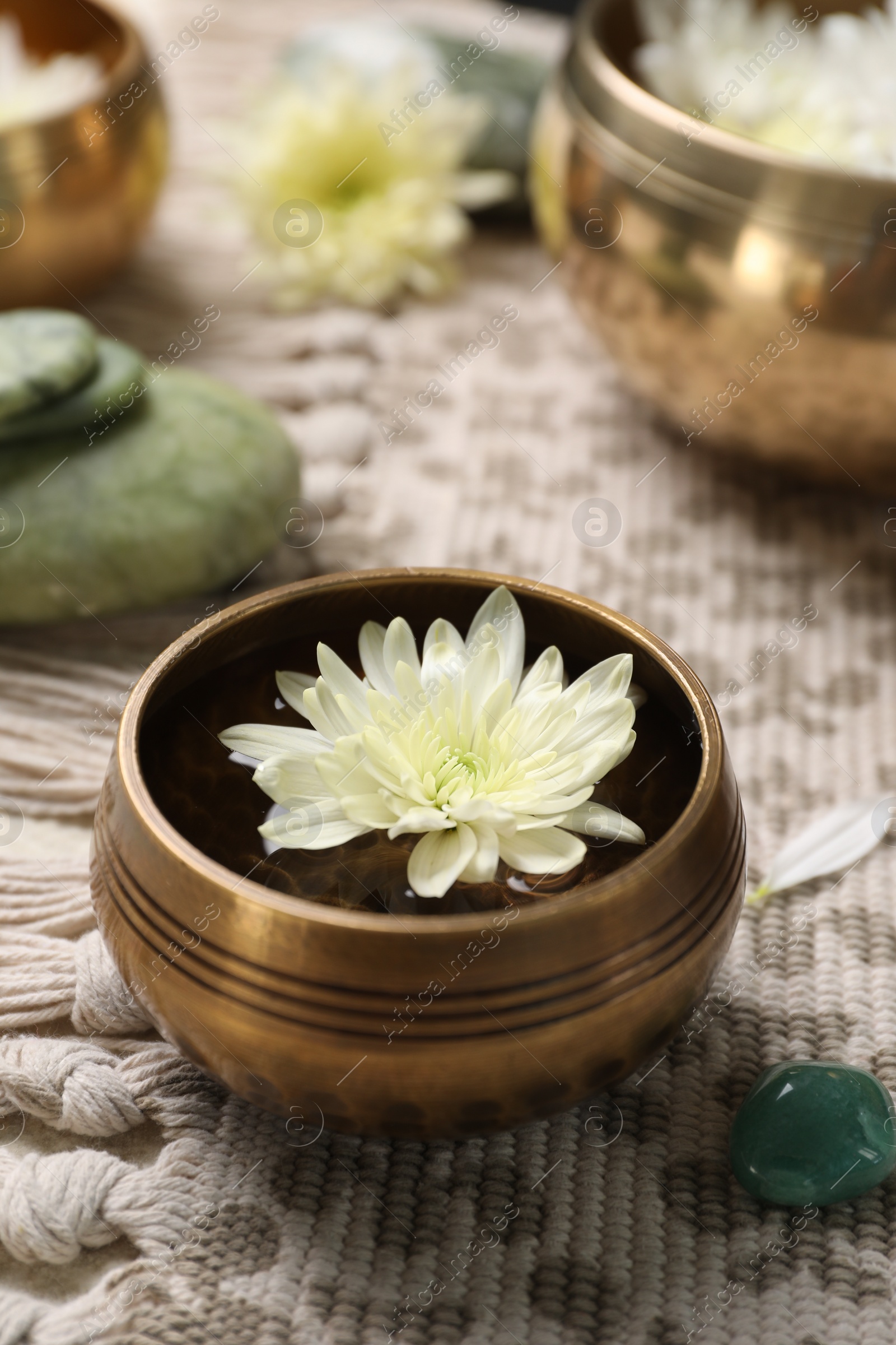 Photo of Tibetan singing bowl with water, beautiful chrysanthemum flower and stones on table