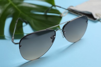 Photo of Stylish elegant sunglasses on light blue background, closeup