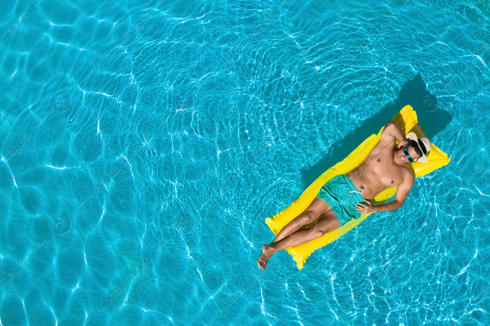 Image of Young man with inflatable mattress in swimming pool, top view. Space for text