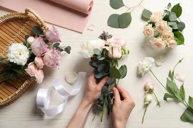 Photo of Florist creating beautiful bouquet at white table, top view