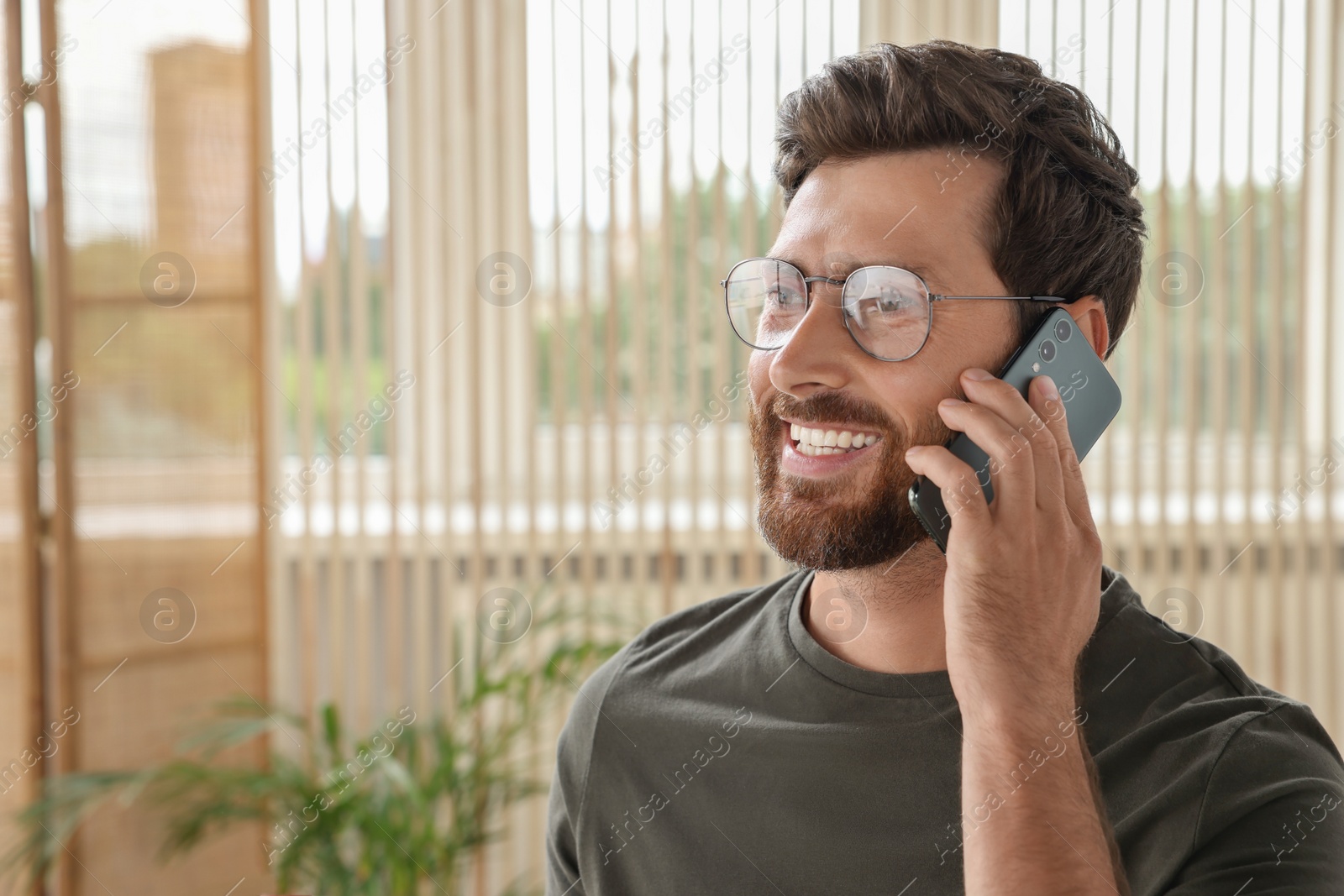 Photo of Handsome man talking on smartphone at home, space for text