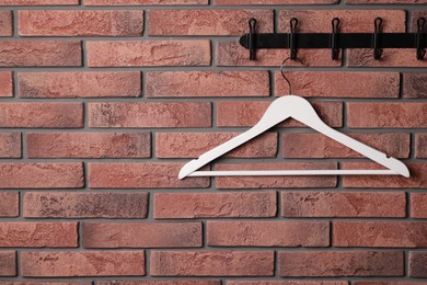 Photo of Hook rack with white clothes hanger on red brick wall. Space for text