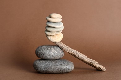 Photo of Stack of stones balancing on wooden stick against brown background. Harmony concept