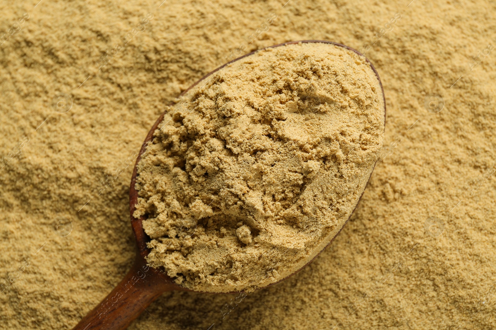 Photo of Heap of aromatic mustard powder and wooden spoon, top view