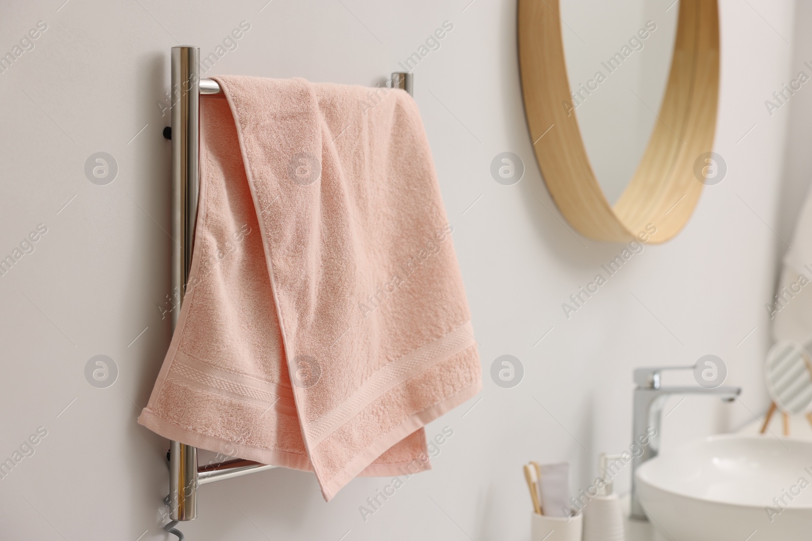 Photo of Heated rail with pink towel on white wall in bathroom