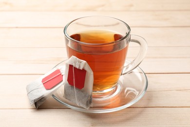Tea bags and glass cup of hot beverage on light wooden table, closeup