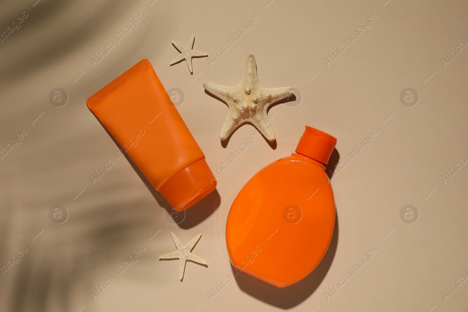 Photo of Sun protection products and starfishes on beige background, flat lay