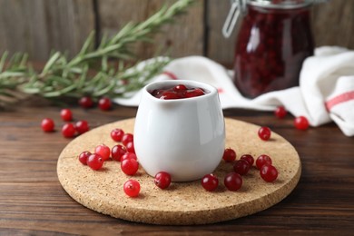 Photo of Cranberry sauce in pitcher, fresh berries and rosemary on wooden table