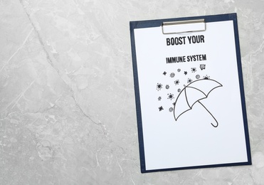 Photo of Clipboard with words Boost Your Immune System and drawing of umbrella on light grey table, top view. Space for text