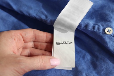 Woman holding clothing label in different languages on blue garment, closeup