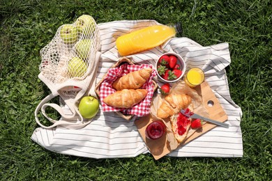 Photo of Blanket with different products on green grass, top view. Summer picnic